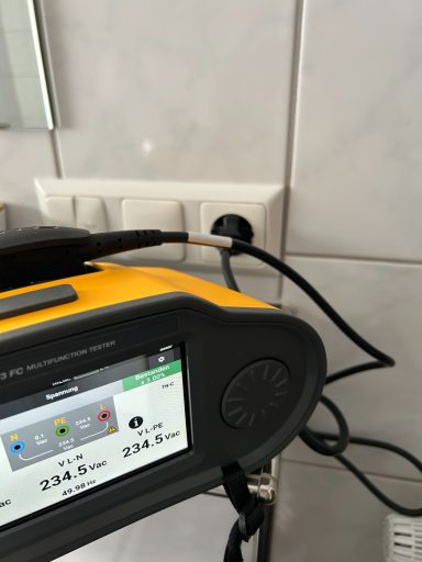 E-Check einer Wohnung Ein gelbes Gerät mit Display und Stecker, das an eine Wandsteckdose angeschlossen ist.